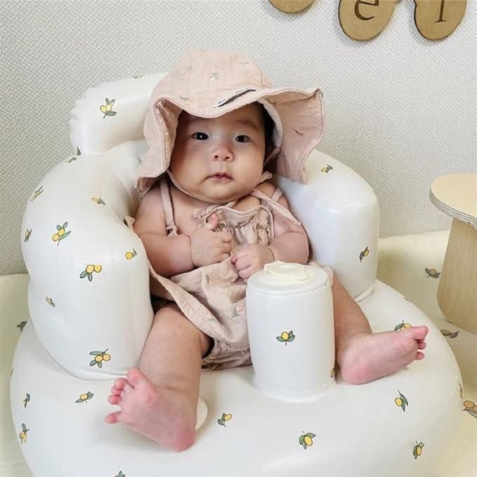 Baby sitting on a white cushion with a pink hat, surrounded by decorative elements.
